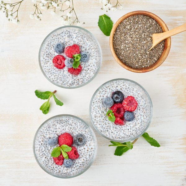 Chia pudding, top view, fresh berries raspberries, blueberries. Three glass, light wooden background, flowers, close up